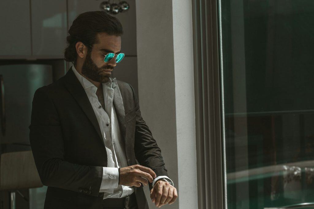 man wearing black coat over white dress shirt fixing his cuffs
